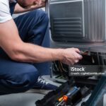 partial view of repairman in working overall fixing refrigerator by screwdriver in kitchen